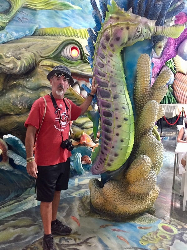 a man poses by a seahorse in a room filled with fake fish at the crazy house