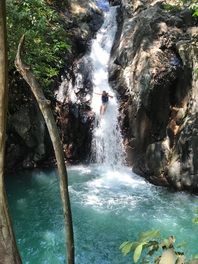 A man slides down a natural rock slide waterfall in Bali