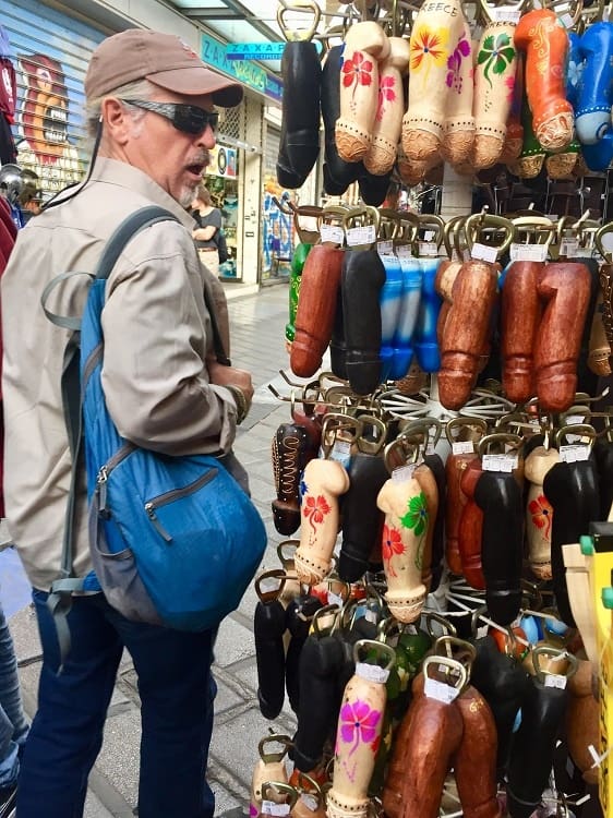 a man walks by a souvenir stand with penis bottle openers of all shapes and colors