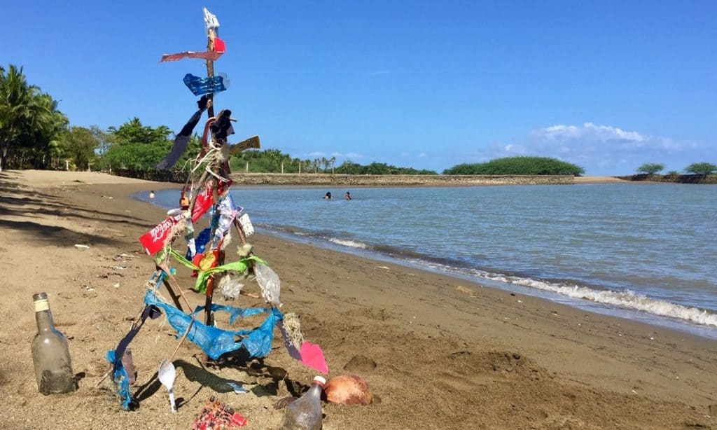 trashy christmas tree on a beach with lots of plastic bits stuck to branches tied together with plastic cords
