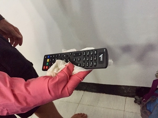 man wearing cleaning gloves holds remote control and an antidisinfectant wipe as part of his travel cleaning kit