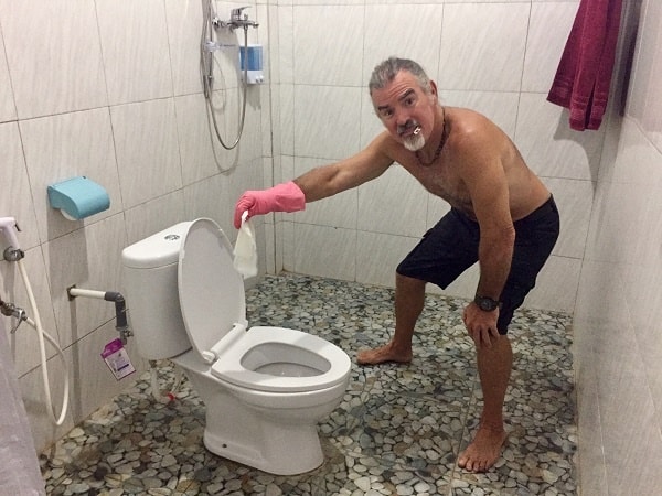 man with rubber gloves holding disinfectant wipe over a toilet as part of his travel cleaning kit