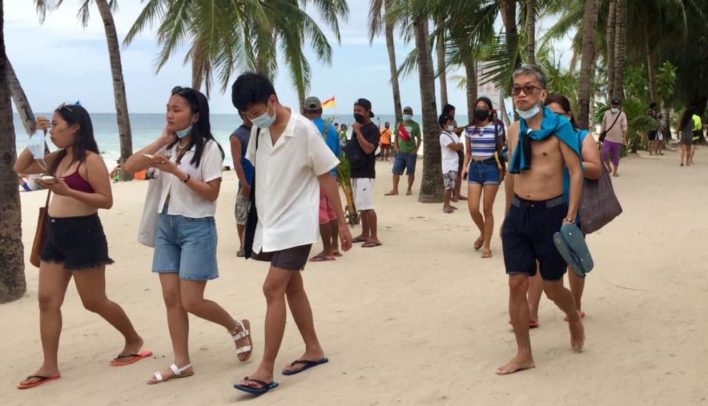 Tourists walk on Boracay's White Beach with masks pulled down under their chins.