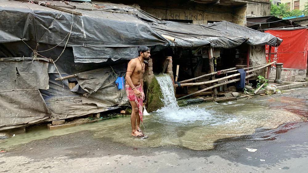 man by burst water main where he bathes in kolkata, india