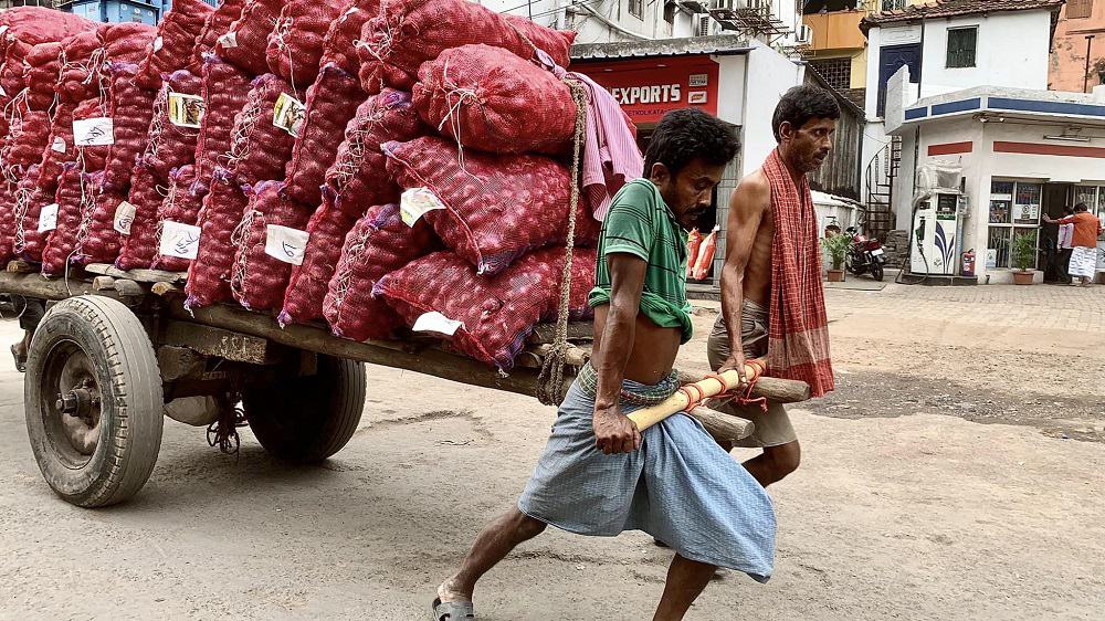 two men pull a car loaded with hundreds of pounds of onions in kolkata, india